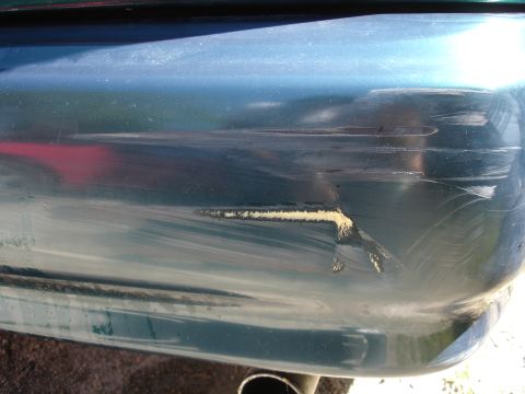 1995 Ford Taurus - Damage to the rear bumper shows deep scratches and chipped paint, revealing underlying material.