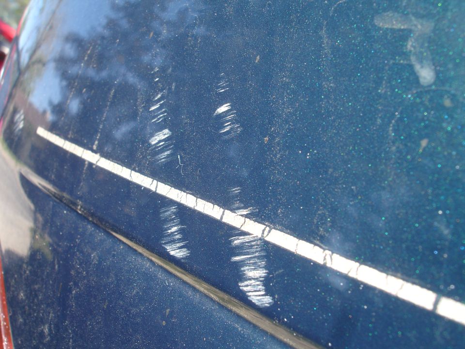 Close-up of a dark blue car panel with many white scratches and a white stripe