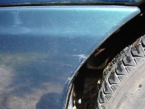 1995 Ford Taurus - Close-up of a damaged teal car fender and tire, with visible scratches and dirt.