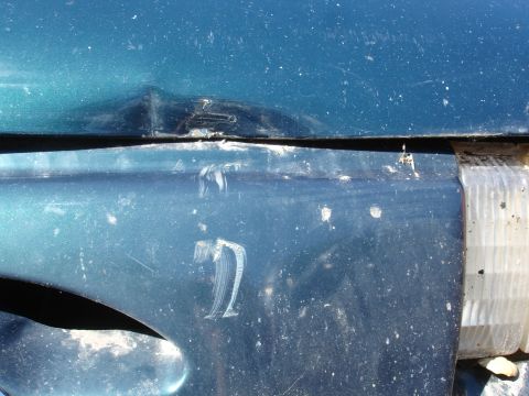1995 Ford Taurus - Close-up of a damaged teal car fender and headlight assembly.