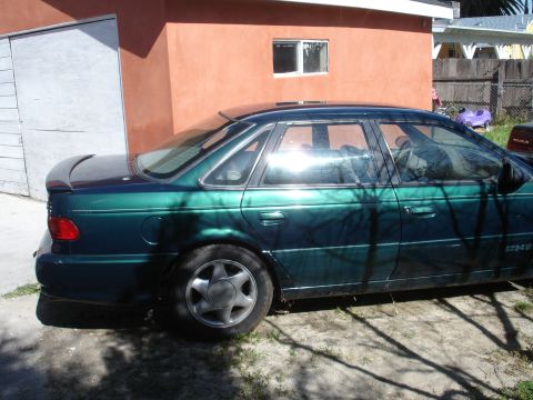 1995 Ford Taurus - A green sedan is parked in front of a building with a fenced yard in the background.