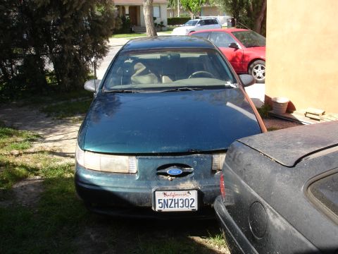 1995 Ford Taurus - A 1995 Ford Taurus is parked in front of a building, with another vehicle to its right.