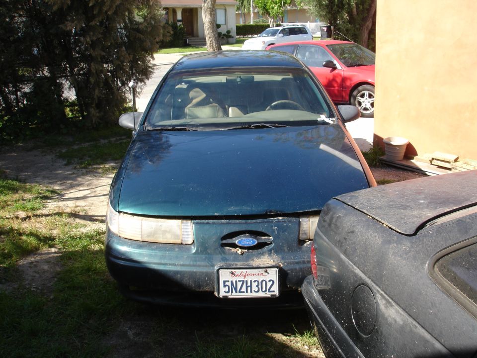 Dark green 1995 Ford Taurus with a California license plate 5NZH302 parked in a driveway