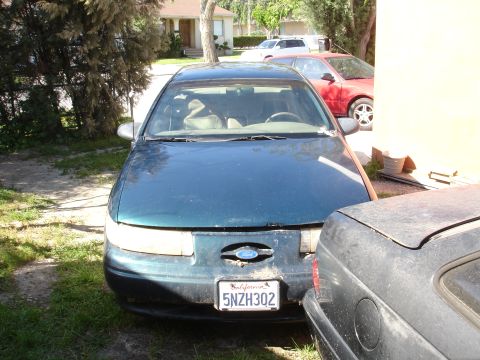 1995 Ford Taurus - A 1995 Ford Taurus is parked in a driveway, partially obscured by another vehicle.