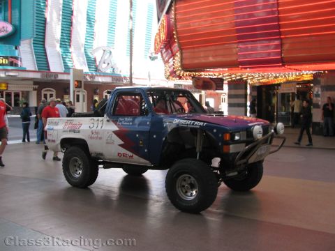1990 Ford Bronco - lifted off-road race truck numbered 311 with patriotic Desert Rat graphics drives along the covered Fremont Street.