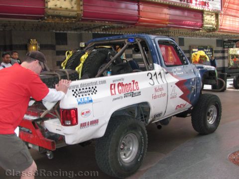 1990 Ford Bronco - man steadies the rear of a lifted off-road race truck numbered 311 showing El CheeZe and Desert Rat sponsor graphics.