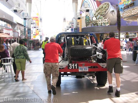 1990 Ford Bronco - Two men push a blue off-road race truck numbered 311 along a covered downtown pedestrian mall lined with casinos.