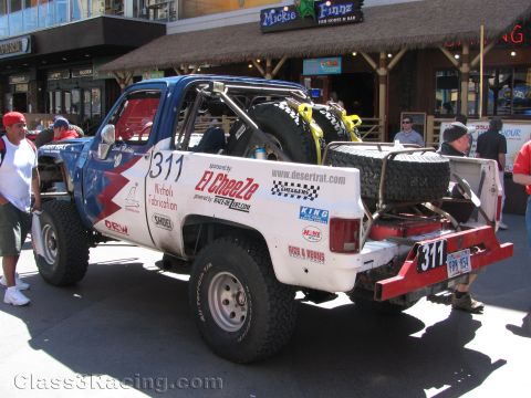 1990 Ford Bronco - sponsor-covered red, white and blue off-road race truck marked 311 sits on pavement in front of a restaurant.