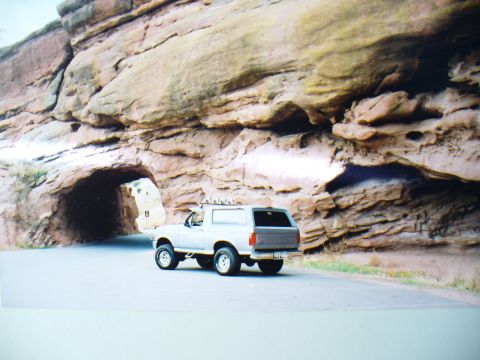 1994 Ford Bronco - 1994 Ford Bronco parked on a road in front of a rock formation with a tunnel.