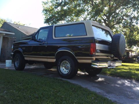 1994 Ford Bronco - This 1994 Ford Bronco is shown from the rear quarter angle, a black body with tan accents and a spare tire mounted on the tailgate.