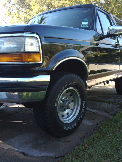 1994 Ford Bronco - A dark blue Ford Bronco is shown from the front quarter angle, parked on a paved surface with grass nearby.