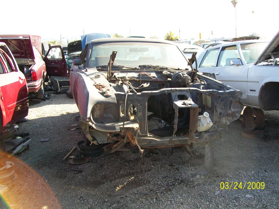 Junkyard scene with a stripped car front end, other cars visible