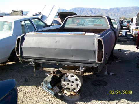 1972 Ford Ranchero - A junkyard scene shows a rear view of a disassembled pickup truck with parts scattered around it.