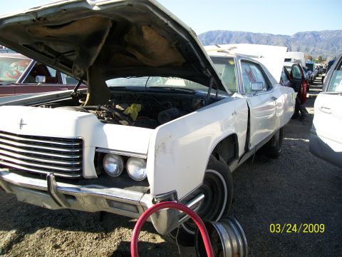 1972 Ford Ranchero - A white sedan, likely from the 1970s, sits in a junkyard with its hood open, revealing the engine compartment.