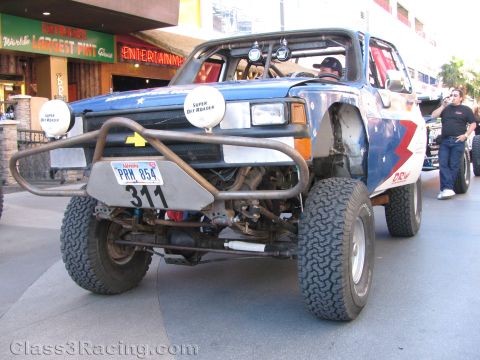 1990 Ford Bronco - Low front view of a blue off-road race truck marked 311 showing its tube bumper, exposed suspension and large tires.