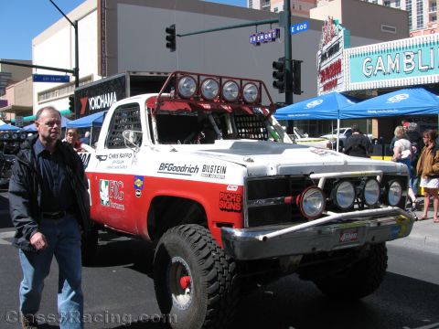 1990 Ford Bronco - man poses next to a red and white off-road race truck with light bar on a downtown street near a Gambling marquee.