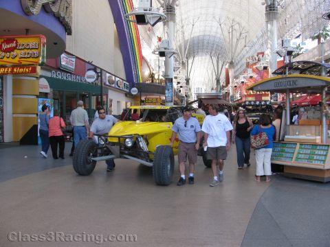 1990 Ford Bronco - yellow off-road race buggy sits in a covered downtown pedestrian mall as people walk past souvenir shops.