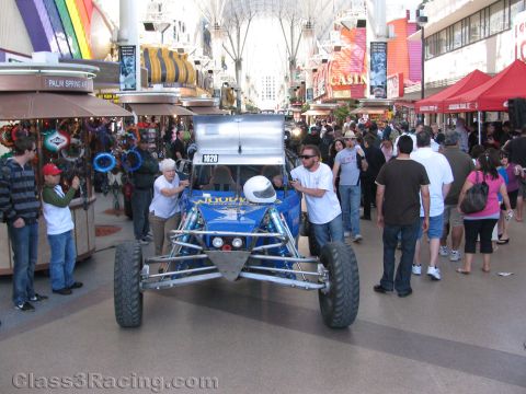 1990 Ford Bronco - blue tube-frame off-road buggy with a helmet on its roll cage is rolled through a crowded covered casino mall.