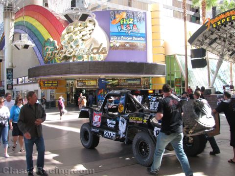 1990 Ford Bronco - black Rockstar-sponsored off-road race truck is moved past the Fitzgeralds casino neon rainbow on a downtown street.