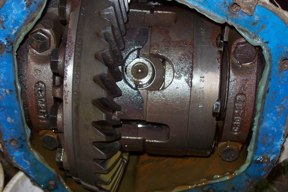 Close-up of differential gears with some blue sealant and oil visible. Part numbers are stamped on the metal