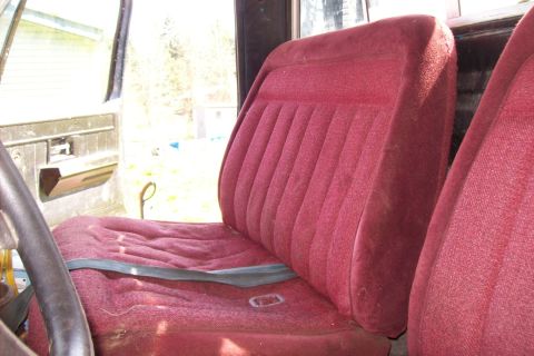 1976 Chevrolet C/K Pickup - The interior of a truck shows a red velour bench seat and door panel, with a steering wheel on the left.