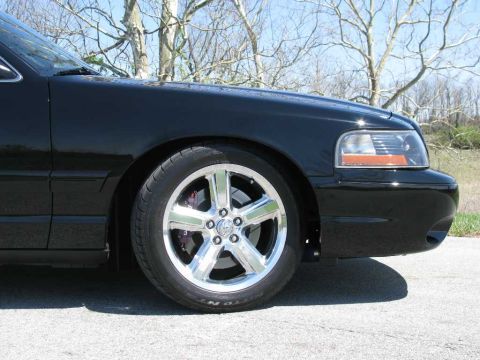 2003 Mercury Marauder - Close-up of a black sedan's front wheel and fender, showing custom chrome rims and red brake calipers.