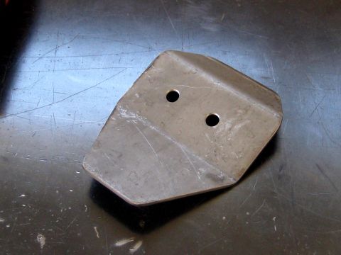 1996 Ford Bronco - A bare steel bracket lying on a scratched shop table, cut to a rounded five-sided shape with a bend across the middle and two drilled holes…