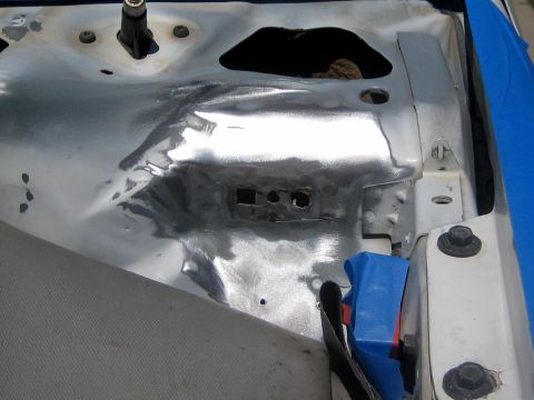 1996 Ford Bronco - Close-up of an inner fender apron stripped to bare metal, with the paint ground off around a bracket mounting area and the factory holes an…