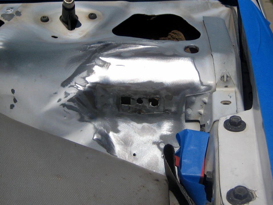 Inner fender apron ground to bare metal around bracket holes, masked with blue tape