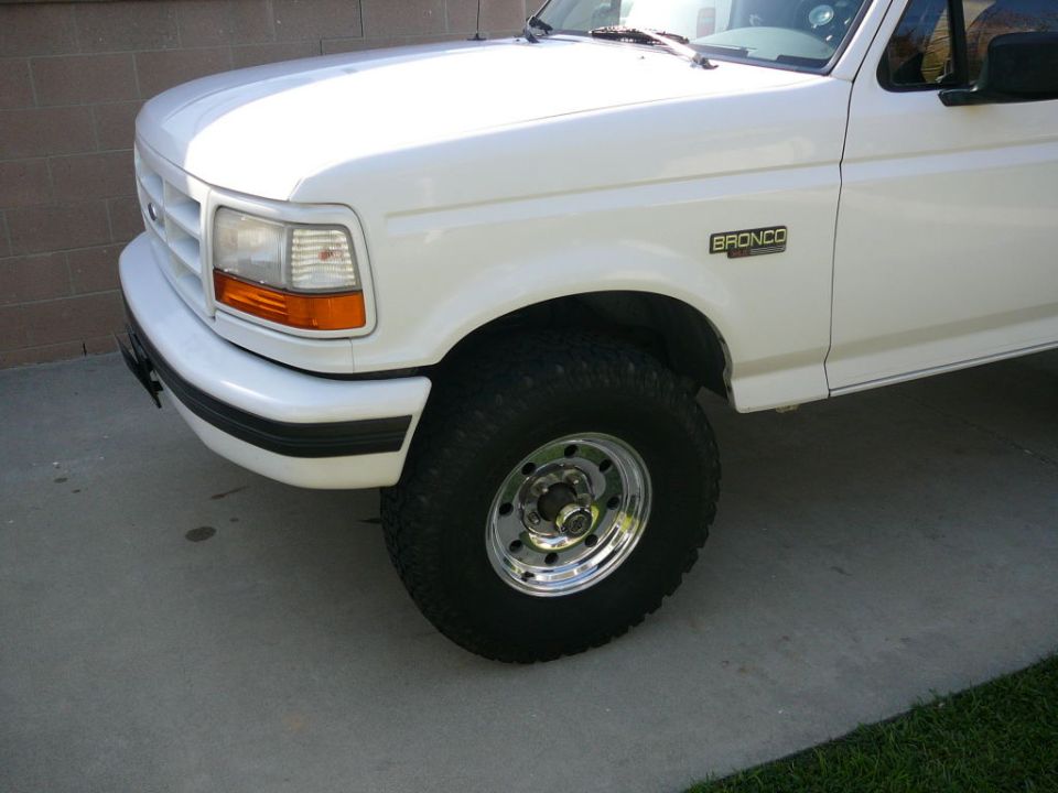 White Ford Bronco parked on concrete, showing front fender and wheel