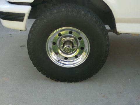 1988 Ford Bronco - Close-up of a white SUV's front fender and wheel, a chrome rim and off-road tire.