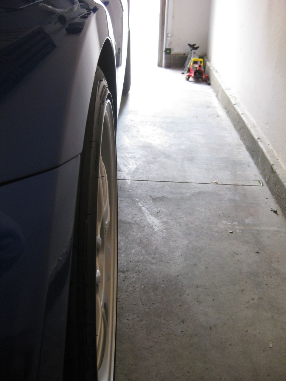 Low-angle side shot of a dark blue lowered car's silver aftermarket wheel in a garage