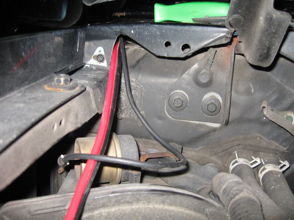 Close-up of engine bay showing red and black wires, hoses, and metal brackets