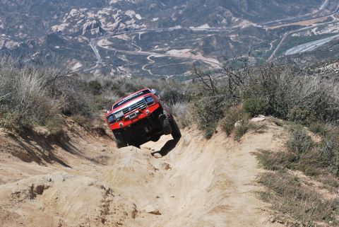 1996 Ford Bronco - A red off-road truck navigates a challenging descent on a dusty mountain trail.