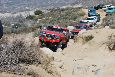 1996 Ford Bronco - Several SUVs, including a red Ford Bronco, are off-roading on a steep, rocky path.
