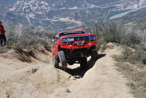 1996 Ford Bronco - A red SUV navigates a steep, rocky trail in a mountainous, arid landscape.