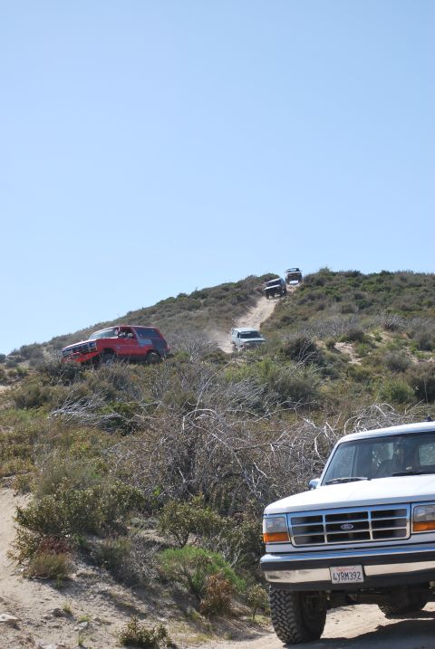 1996 Ford Bronco - Several SUVs navigate a dusty, off-road trail on a sunny day.