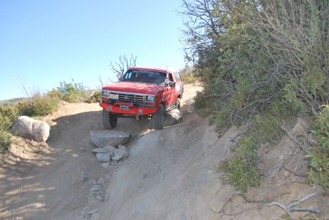 1996 Ford Bronco - Off-road Bronco navigating a rocky trail with brush and trees in the background.