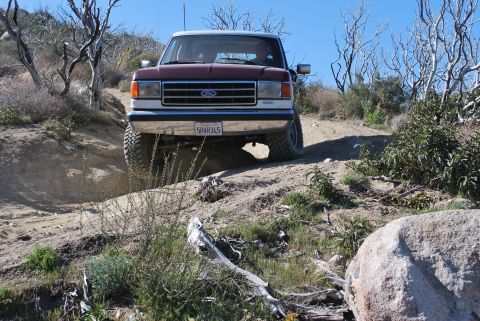 1996 Ford Bronco - A maroon and white Ford Bronco navigates a rocky, off-road trail under a clear blue sky.