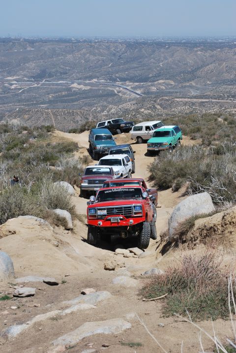 1996 Ford Bronco - A line of off-road vehicles navigates a rocky mountain trail under a clear sky.