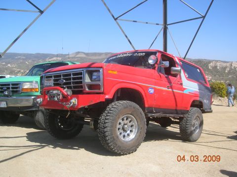 1985 Ford Bronco - Modified red Ford Bronco and a green Ford truck parked outdoors on a sunny day.