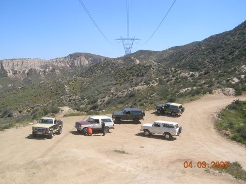 1985 Ford Bronco - A group of SUVs, including a 1985 Ford Bronco, are parked on a dirt road in a scenic, mountainous area.