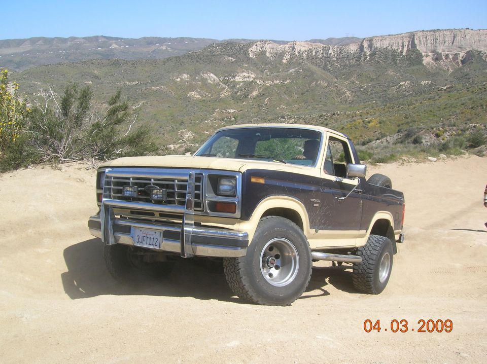 Ford Bronco parked on dirt road with mountains in background. License plate reads 3JFT112