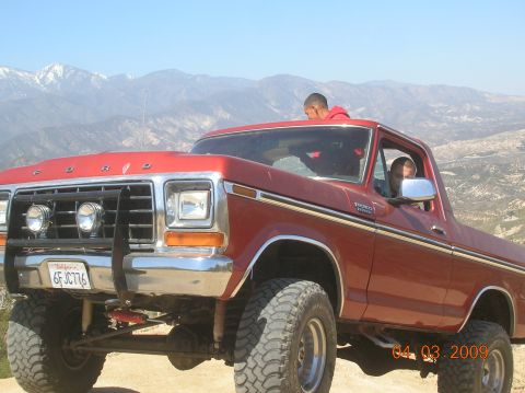 1985 Ford Bronco - A red Ford Bronco is seen off-road with mountains in the distance.
