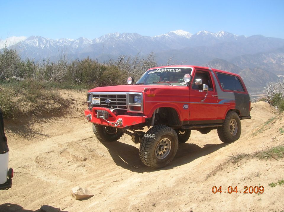 Red 1985 Ford Bronco with off-road modifications on a dirt trail
