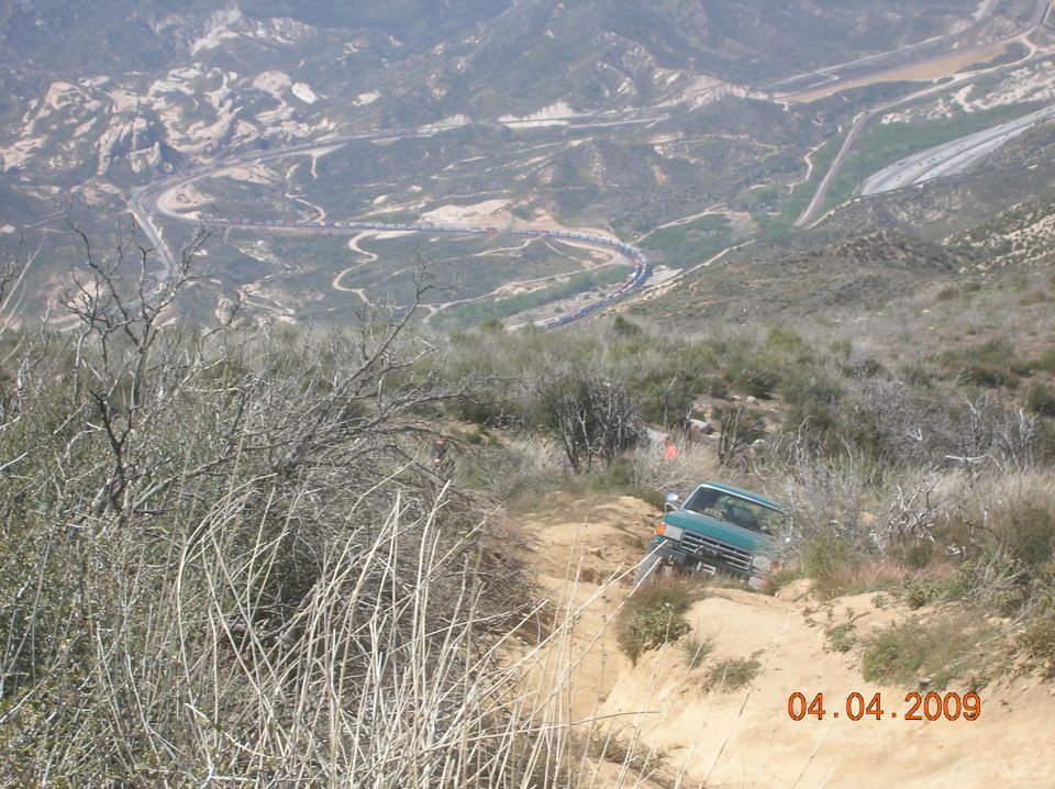 Green pickup truck on a dirt trail, angled to the right, with a mountainous landscape in the background