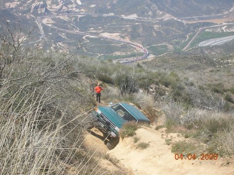 1985 Ford Bronco - A green SUV is stuck on a steep, rutted dirt trail, with a person observing the situation.