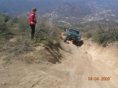 1985 Ford Bronco - A green SUV navigates a challenging off-road trail with a person watching from the side.