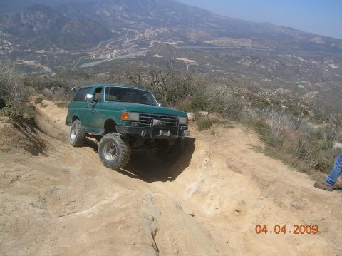 1985 Ford Bronco - This green SUV navigates a challenging off-road trail with steep inclines and rocky terrain.