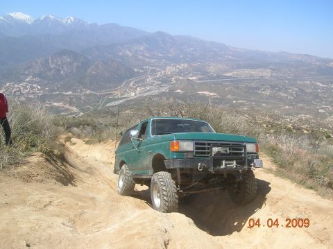 1985 Ford Bronco - Ford Bronco navigates a challenging off-road trail with a scenic mountain vista.